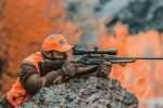 Hunter in blaze orange shouldering a scoped Benelli Lupo rifle off a rock with autumn aspens behind him